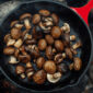 Sizzling mushrooms cooking in a cast iron skillet over an open f